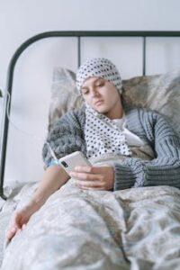 A cancer patient in bed using a smartphone, symbolizing hope and resilience.